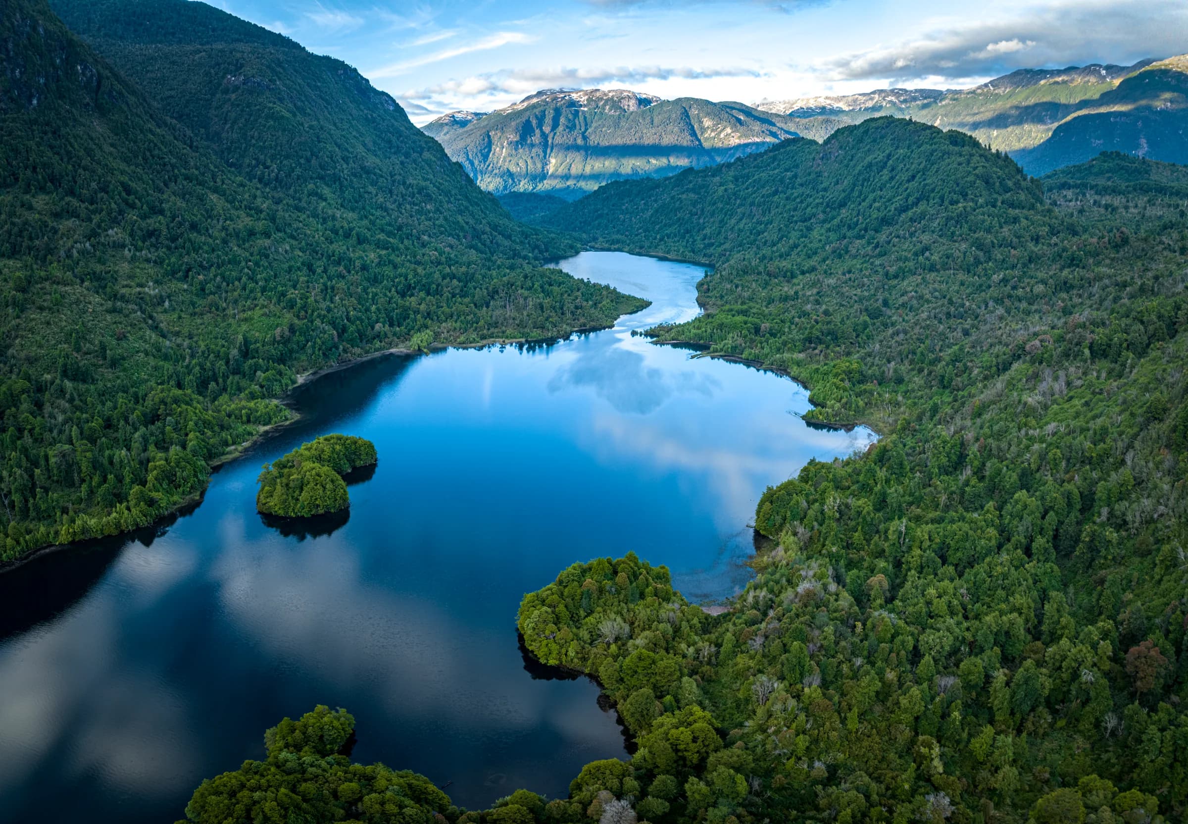 Aerial sweep of Lago Roosevelt under a clear sky, forest meeting deep blue water